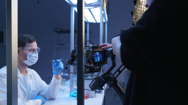 A professional camera shooting an actor in a role of a scientist in a laboratory. Backstage from filming a movie of a photo set in a laboratory decorations and an operator shoulder in the foreground
